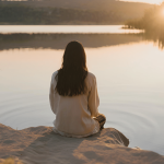 A person sitting near a tranquil lake at sunset, representing peace and recovery after an unmarried separation.